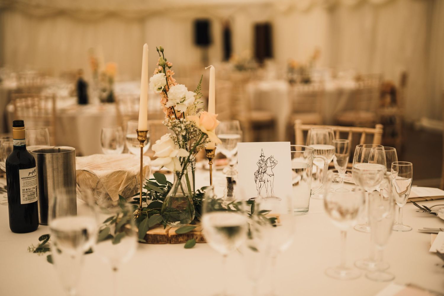 Elegant wedding reception table with floral centerpiece and wine glasses in soft lighting.