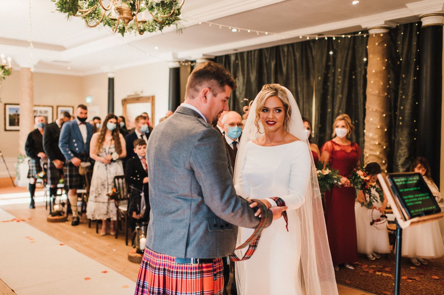 A Scottish wedding ceremony with traditional kilts and white wedding dress in an elegant indoor venue.