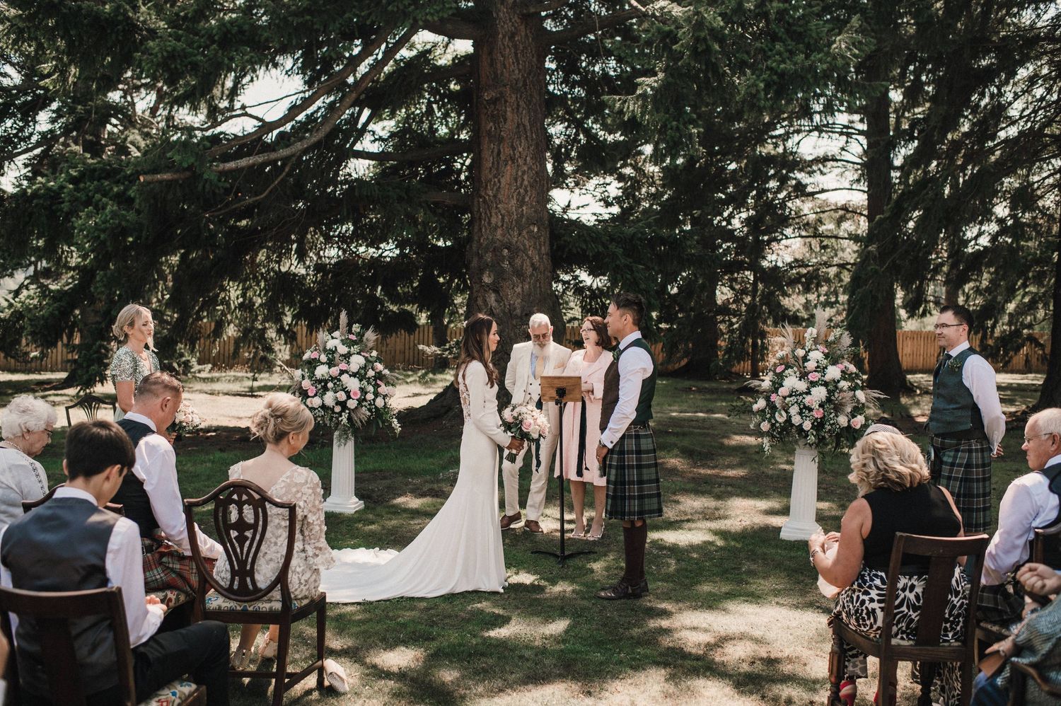 Outdoor wedding ceremony in a serene forest setting with decorated chairs and floral arrangements.