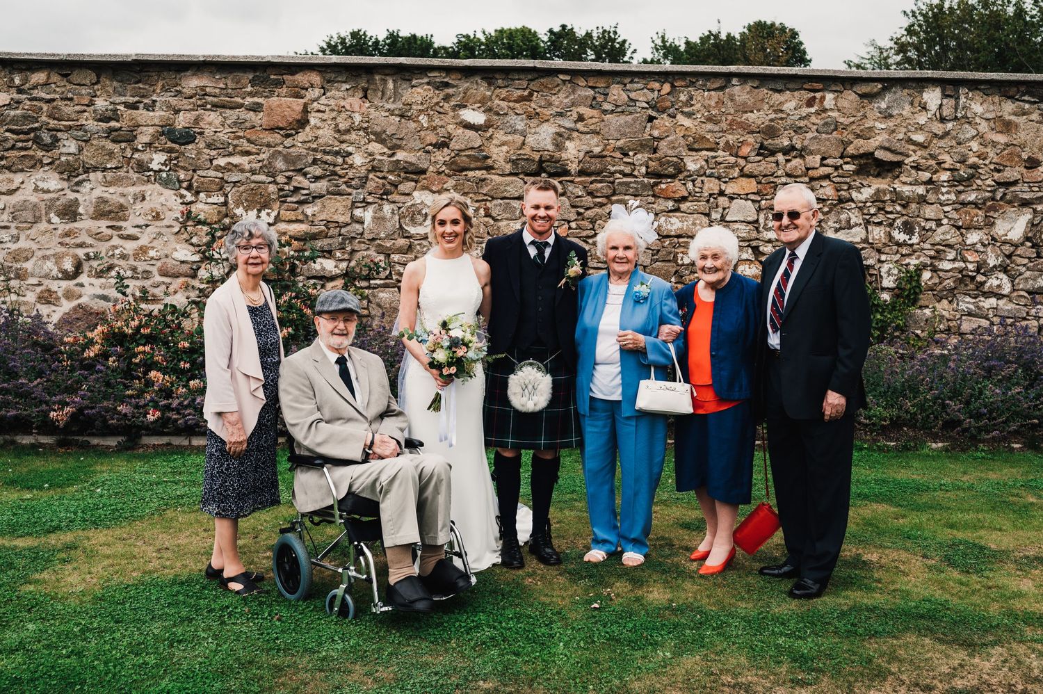 Small wedding group poses for formal portrait against stone wall backdrop.