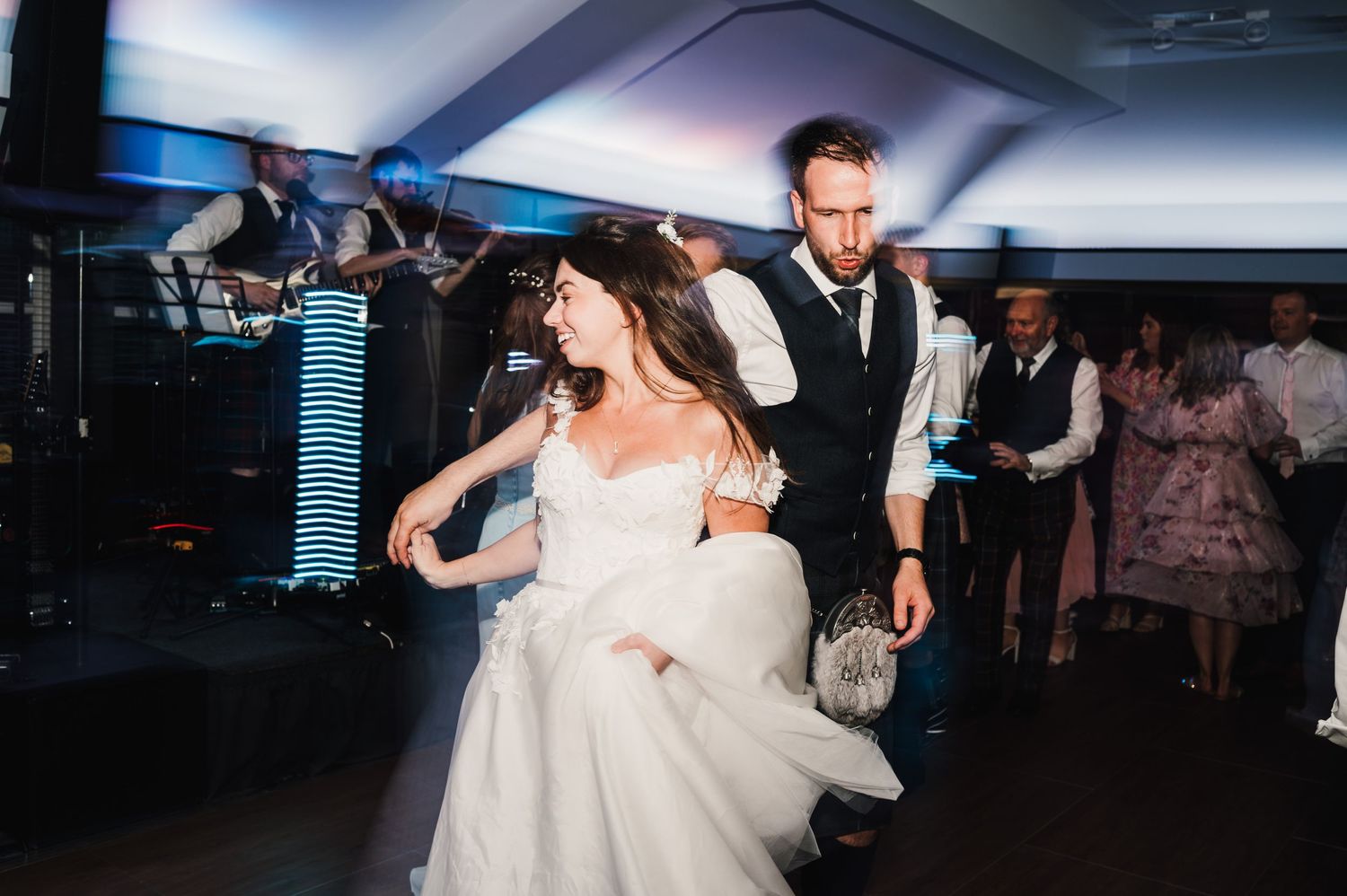 Couple dances energetically during wedding reception in dimly lit venue.