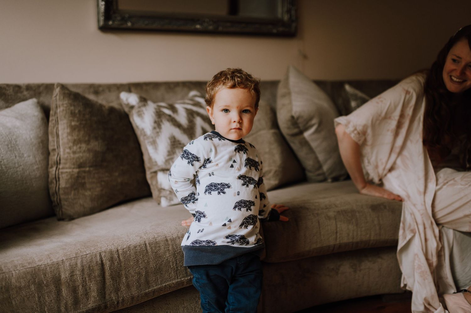 Toddler in animal print sweater standing on gray couch.