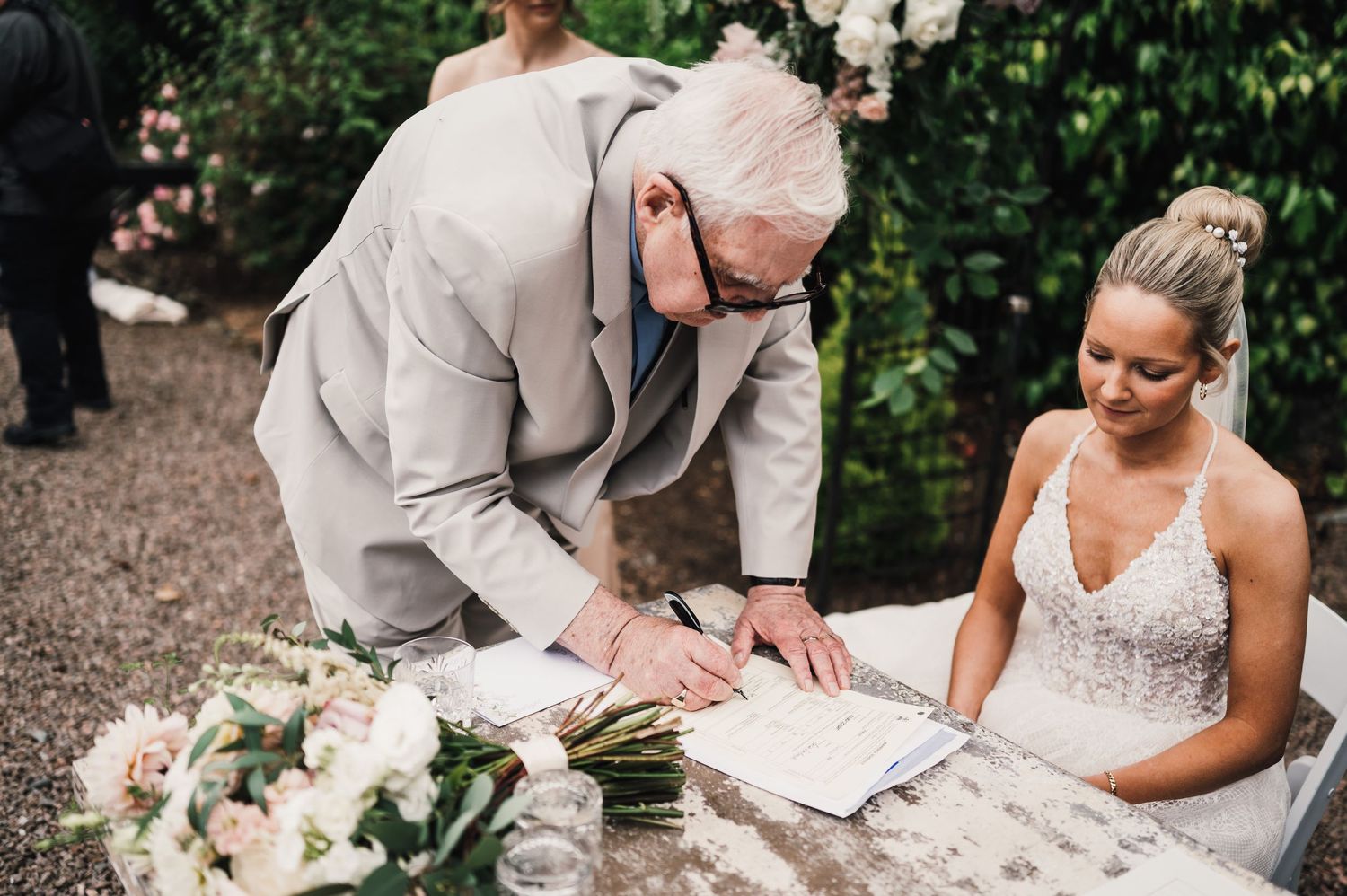 Wedding ceremony signing moment at stone table decorated with floral arrangements.