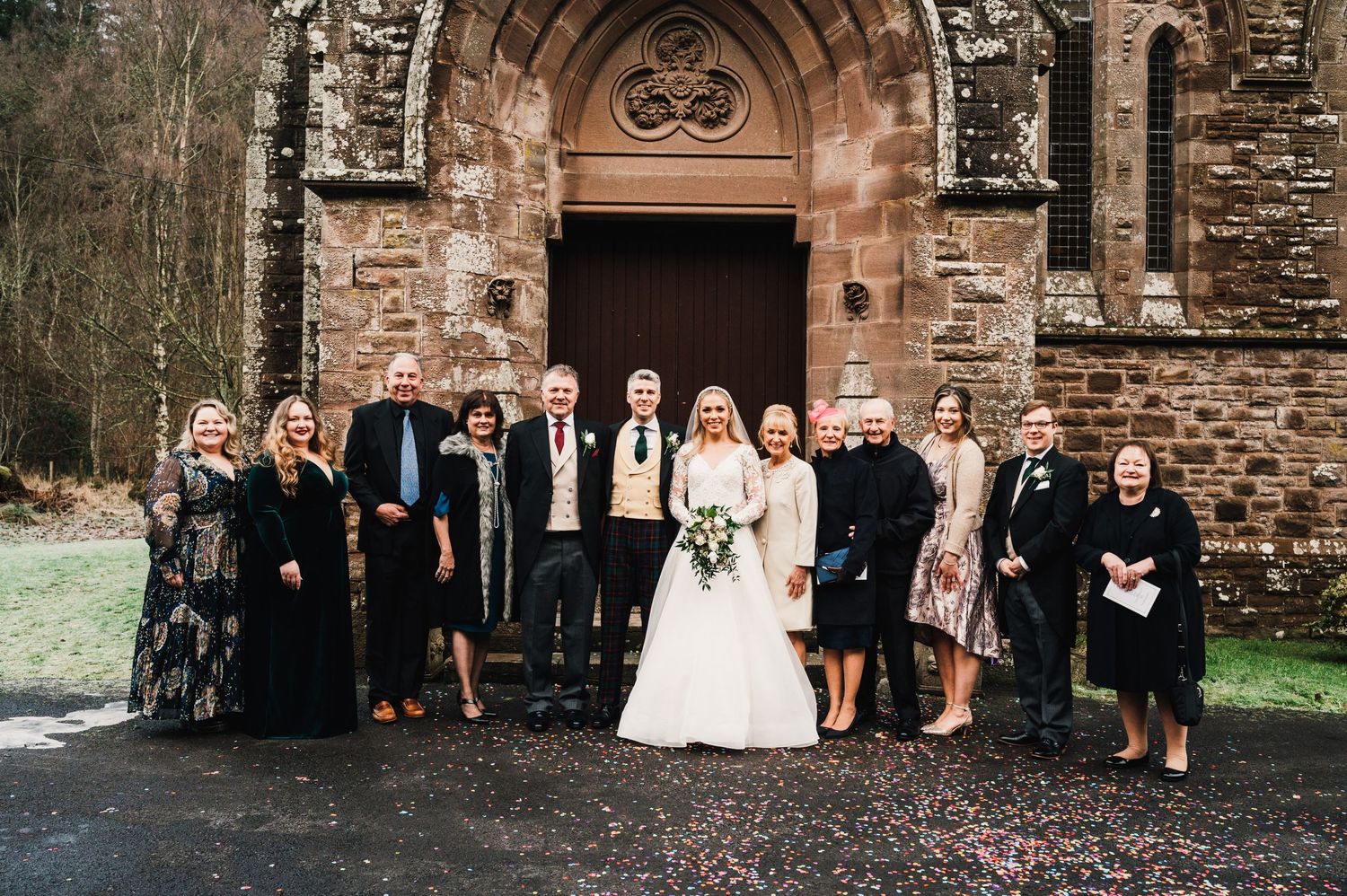 Wedding group portrait in front of a gothic stone church entrance with arched doorway.