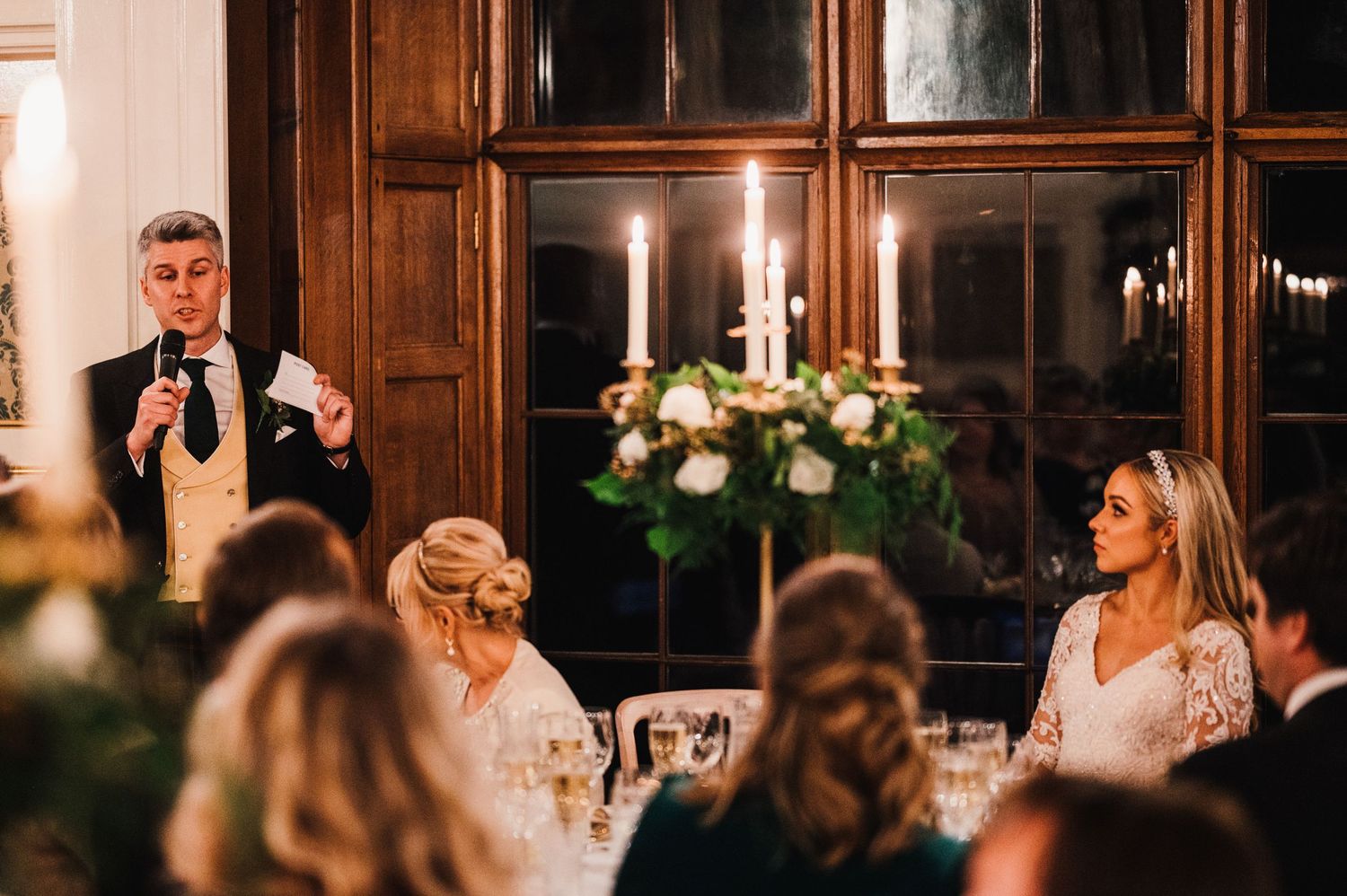 Someone delivers a toast during candlelit wedding reception with wood-paneled walls.