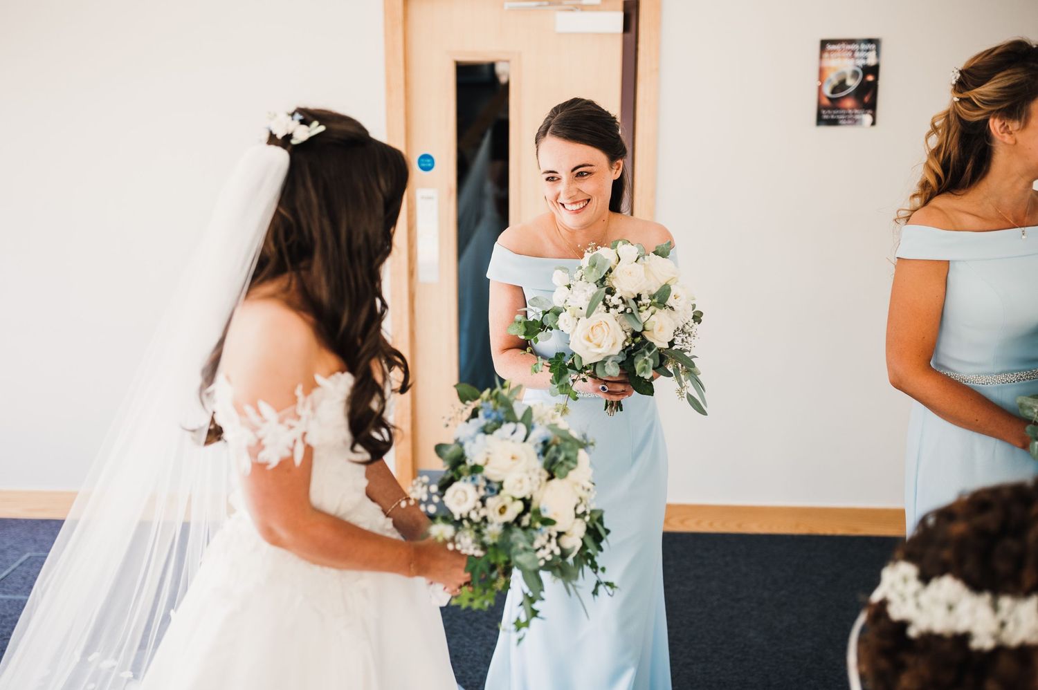 Bridesmaids in light blue dresses admire wedding bouquets during preparation.