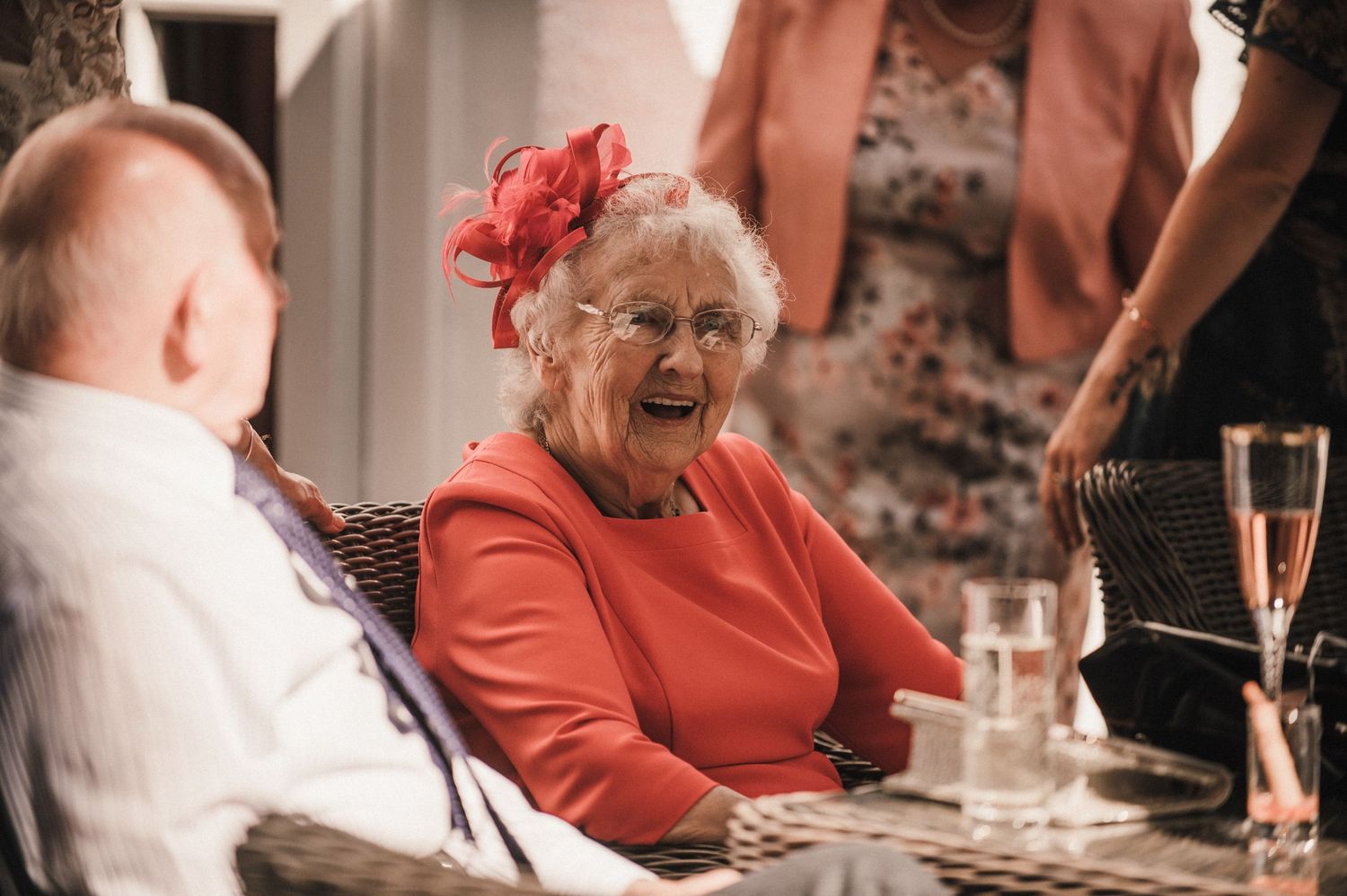 Elderly guest in bright coral dress laughing joyfully at wedding reception.
