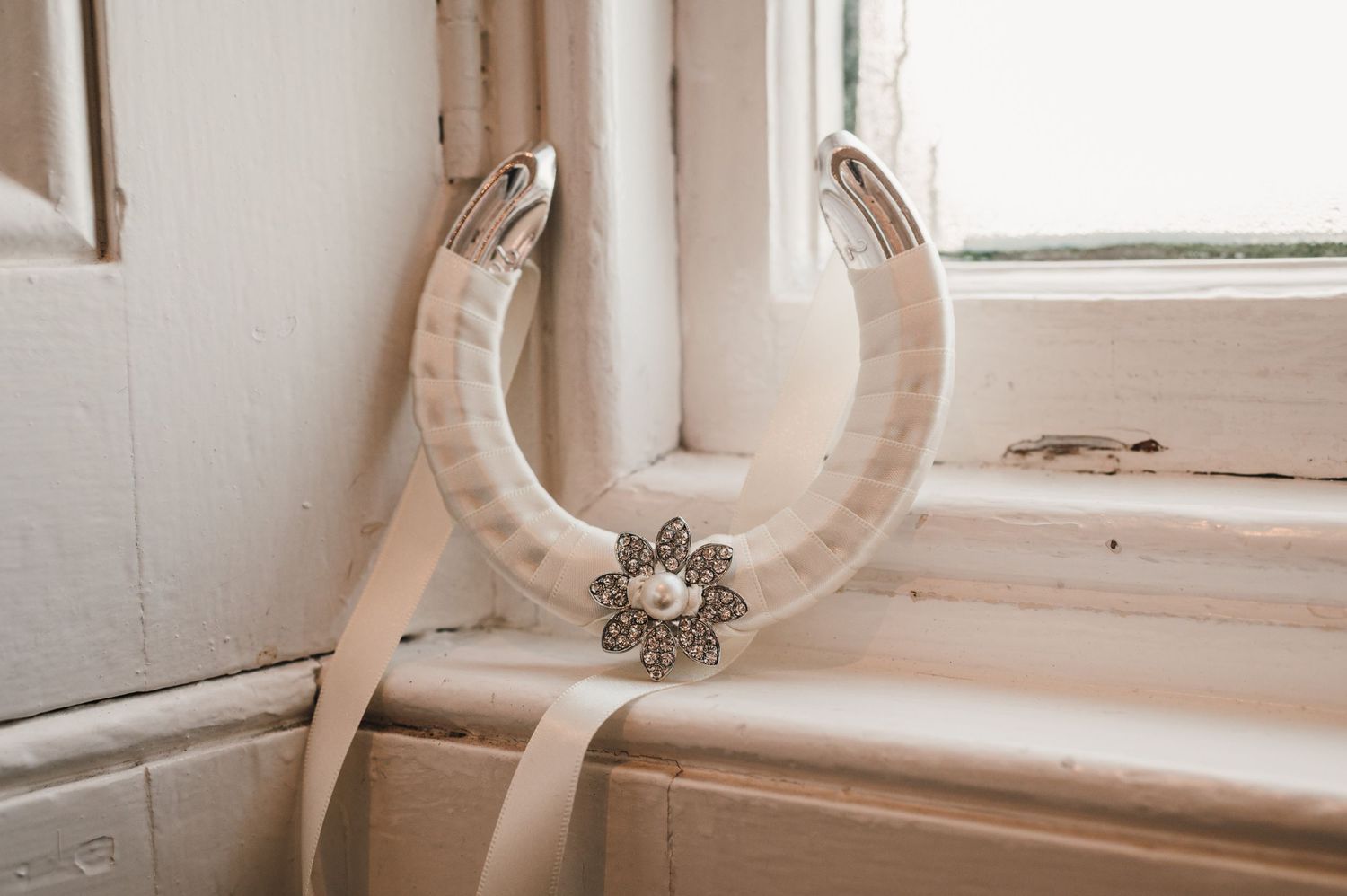 A decorative horseshoe with crystal embellishments displayed on a white windowsill.