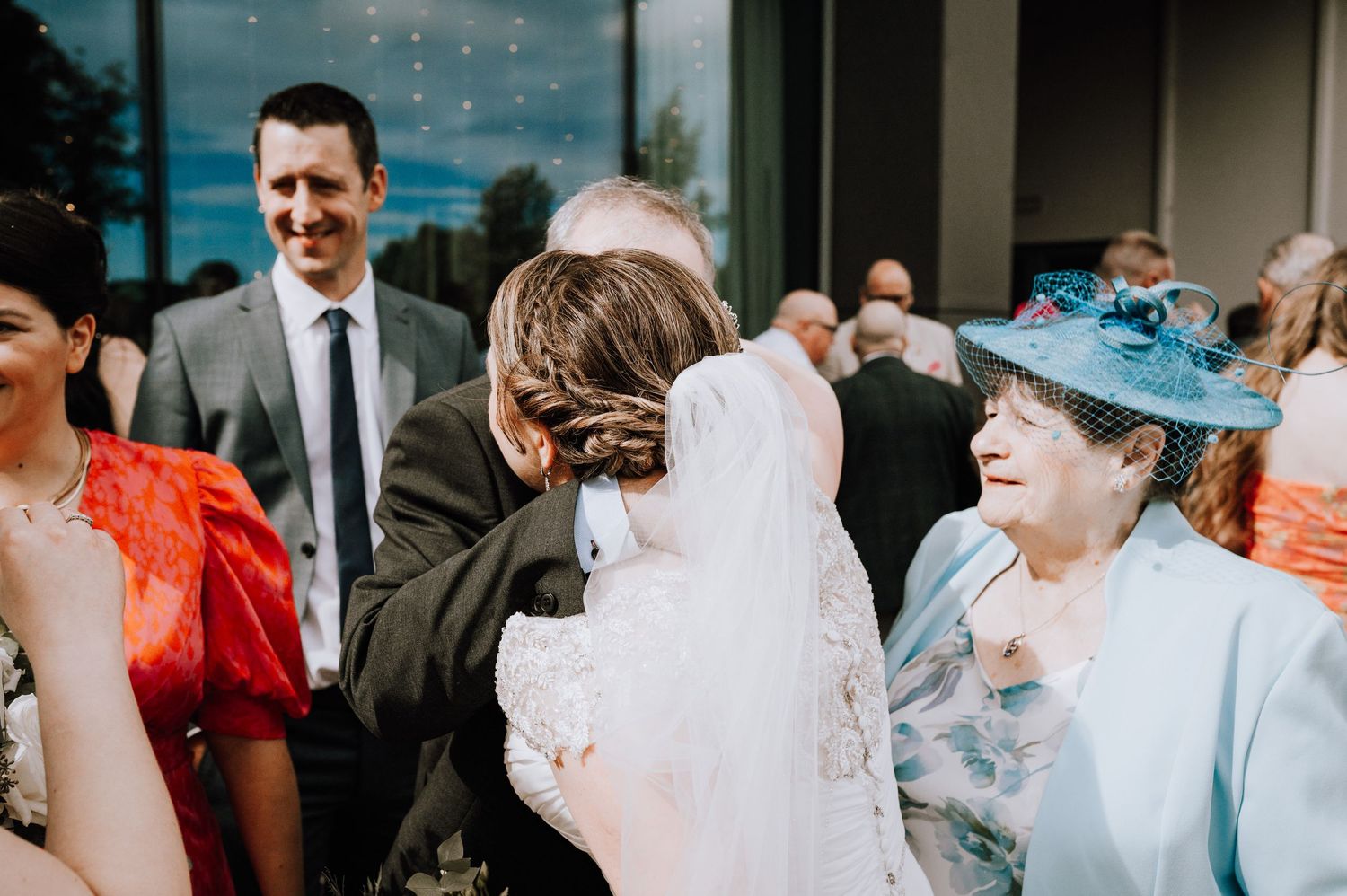 Wedding guests gather outside a modern building during a celebration.