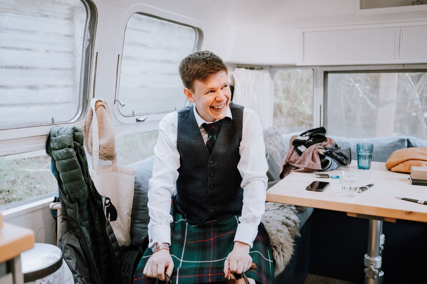 Person in traditional Scottish formal wear smiling while getting ready in mobile changing area.
