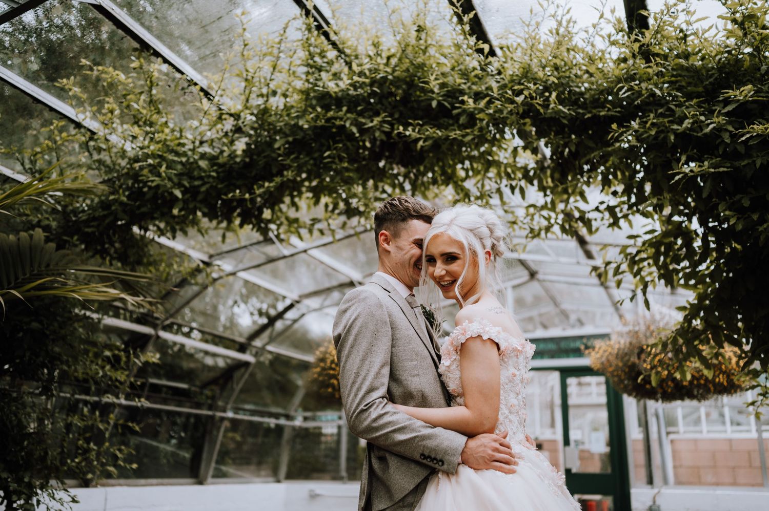 Wedding couple embracing in a romantic greenhouse setting surrounded by foliage.