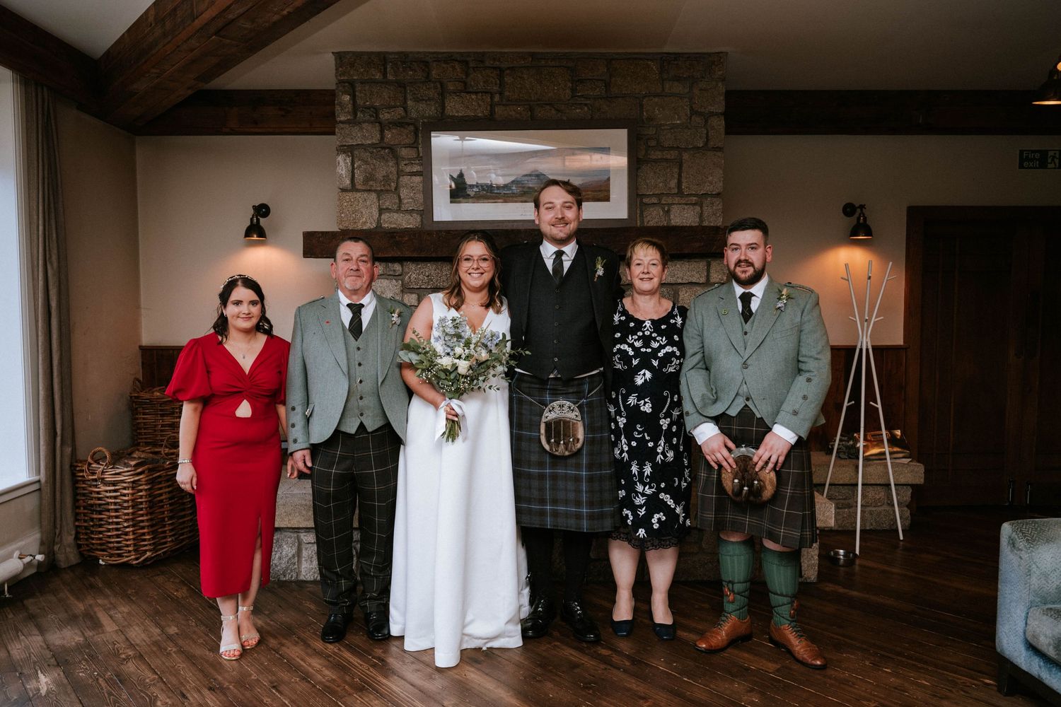 Wedding party members pose together in a rustic indoor venue with exposed brick walls and warm lighting.