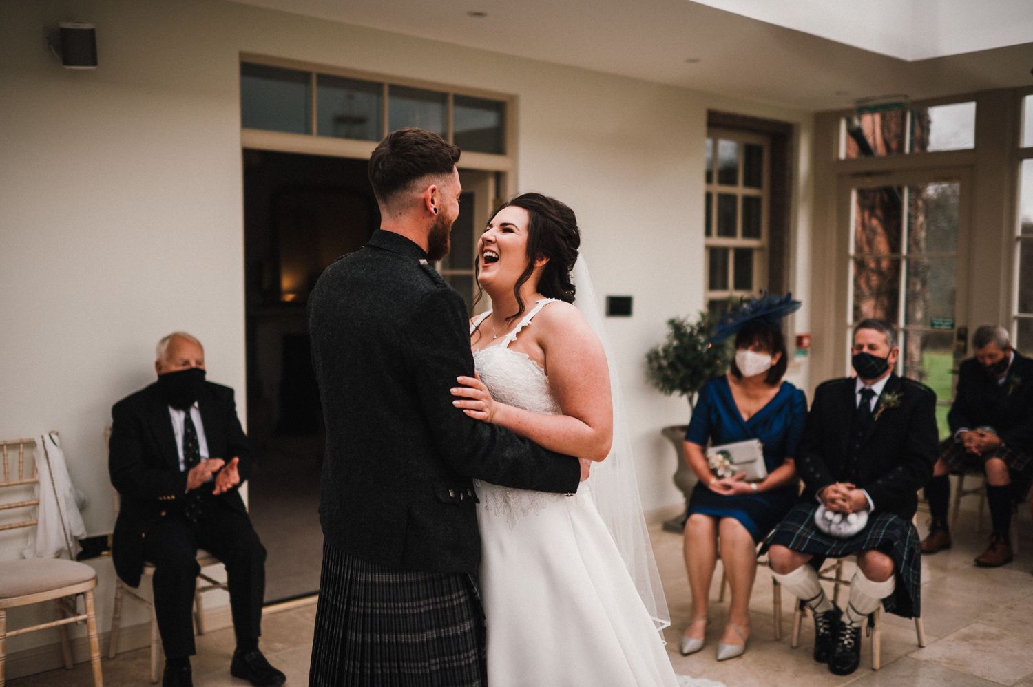 Newlyweds share a joyful moment during their Scottish wedding ceremony while guests look on.