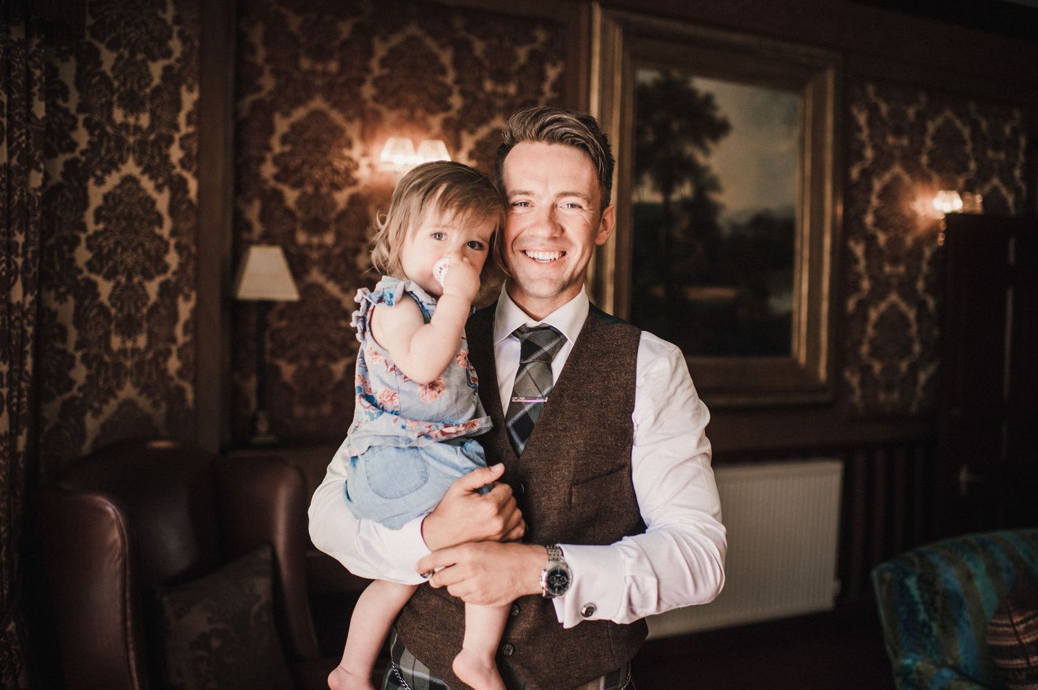 A heartwarming moment captured against ornate wallpaper in formal attire.