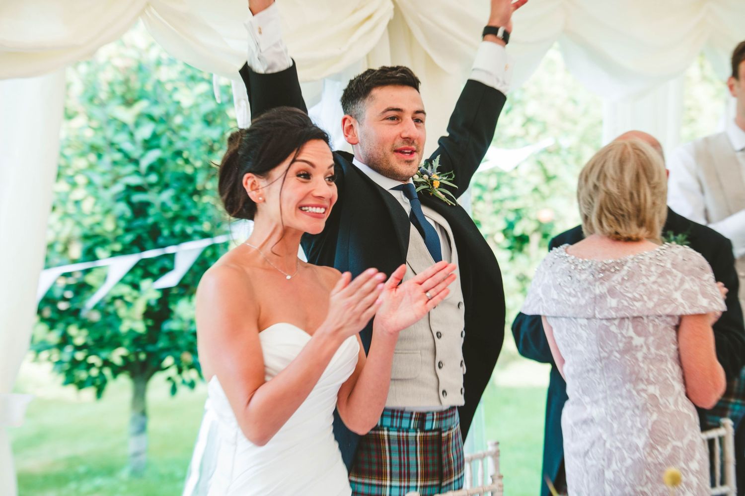 Wedding celebration in a marquee tent with couple celebrating joyfully in traditional Scottish attire.