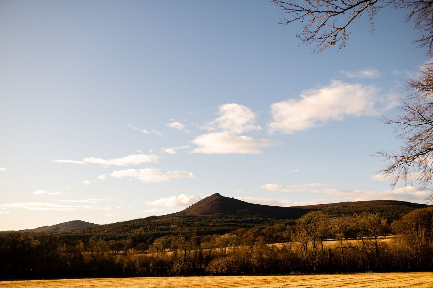 Scenic mountain landscape with rolling hills under blue sky and fluffy clouds.