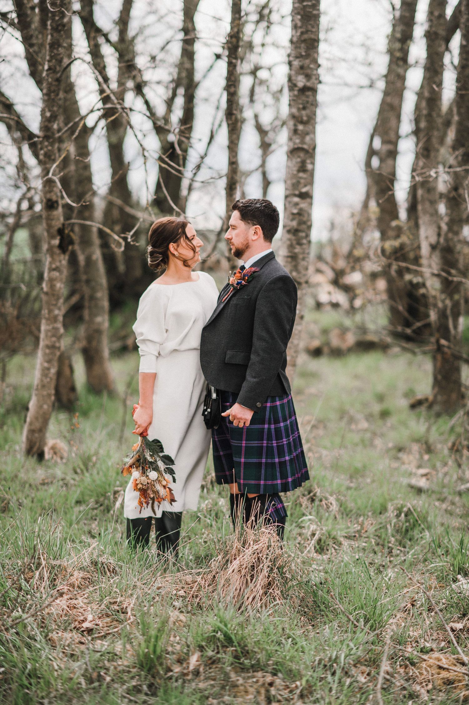 Wedding couple photographed in a woodland setting wearing traditional Scottish wedding attire.