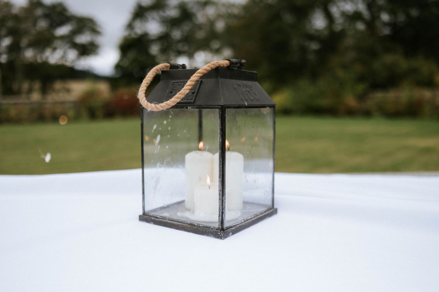 Vintage lantern centerpiece on a white tablecloth at an outdoor wedding reception.