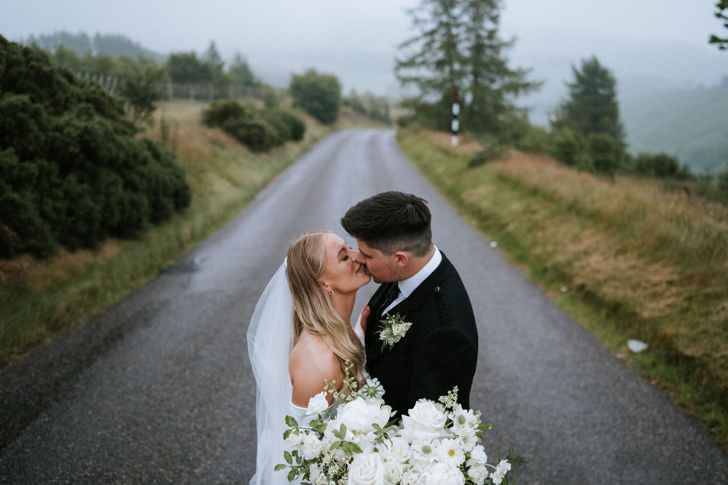 Romantic wedding photos taken on a misty country road surrounded by green scenery.