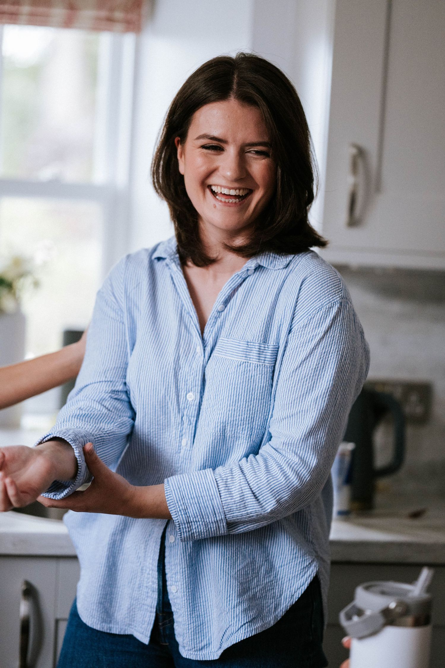 A casual portrait series in a bright kitchen showing joyful expressions in a blue striped shirt.