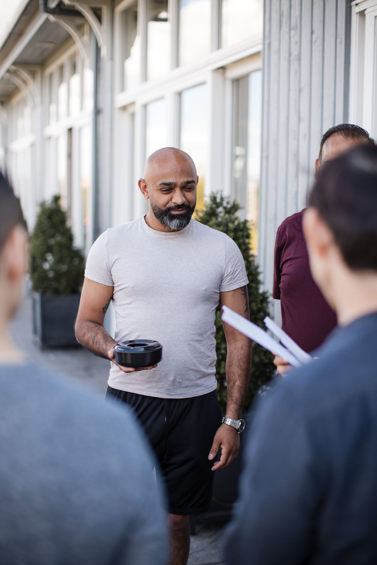 Man in gray t-shirt and dark pants stands in front of white building exterior.