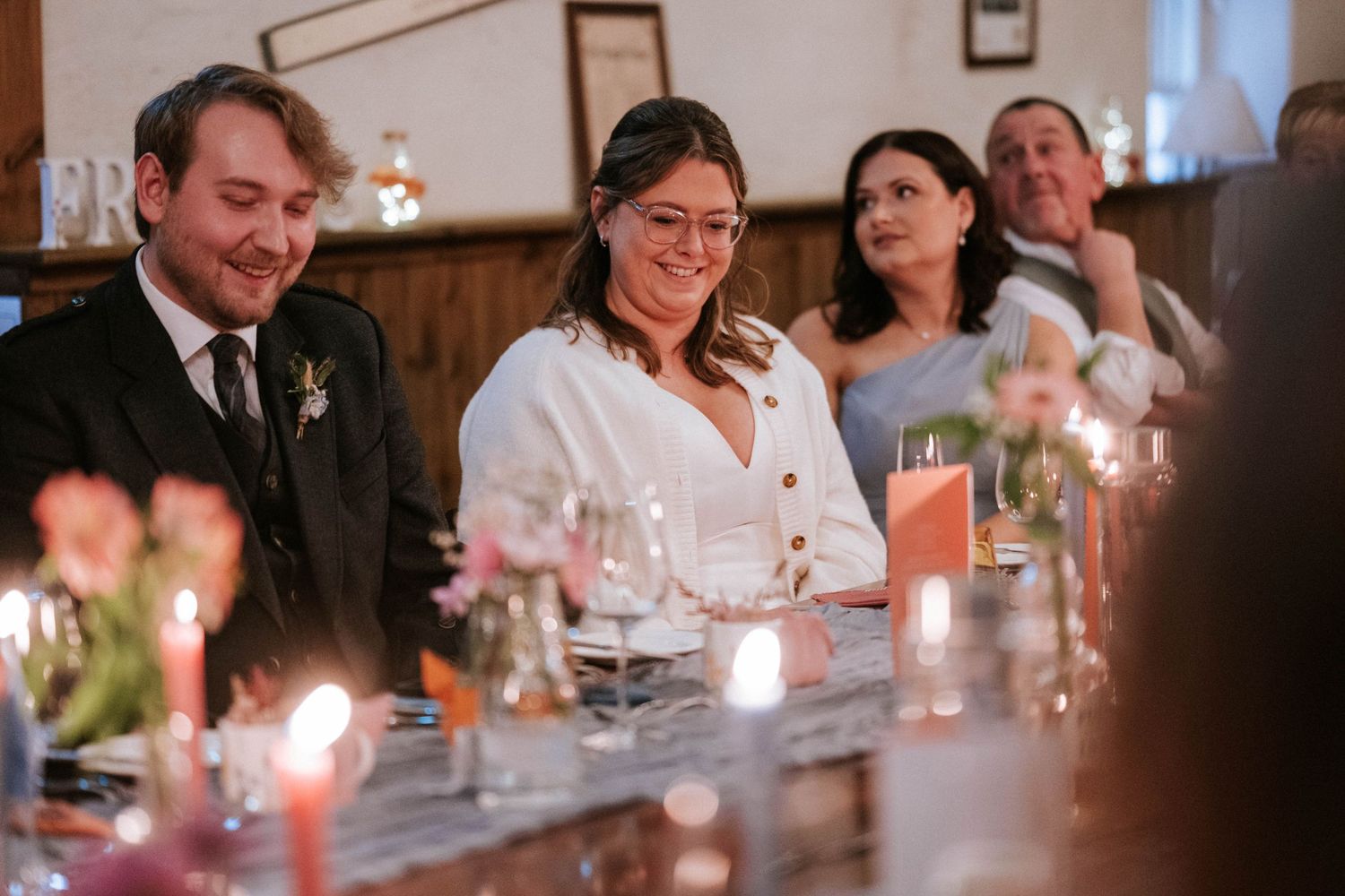 Candlelit wedding reception dinner with guests seated at long tables in a rustic venue.