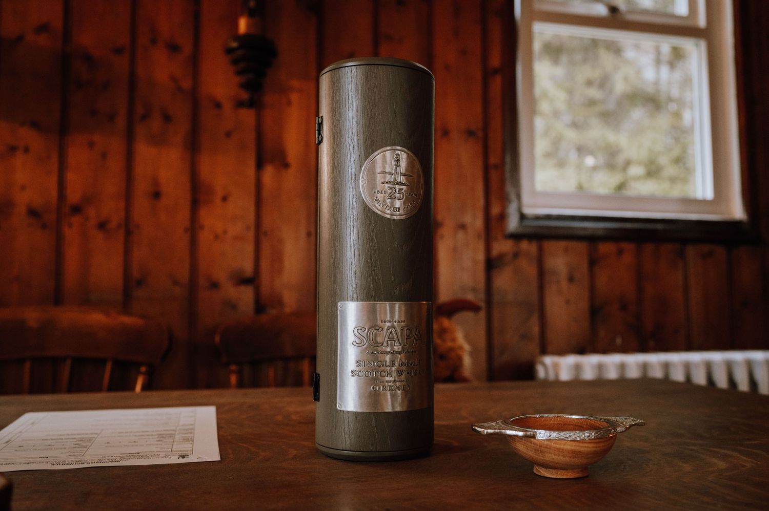 A dark metal tumbler sits on a wooden table next to a small dish.