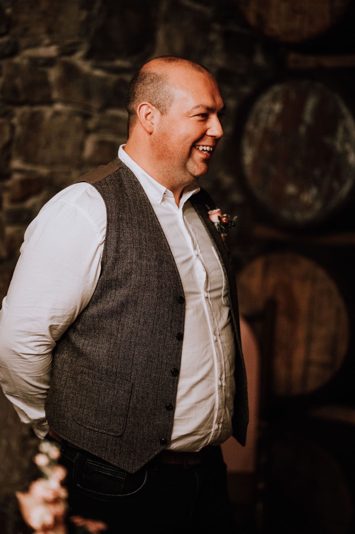 Wedding guest smiling in front of wine barrel wall wearing formal attire.