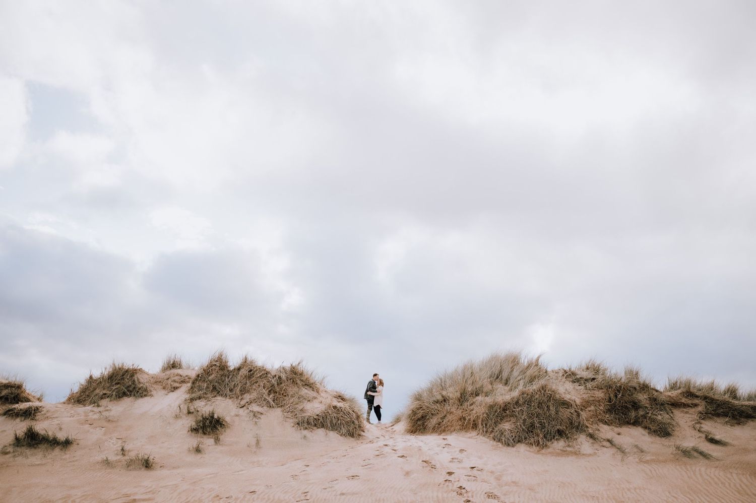 Couple sharing an intimate moment between sand dunes on an overcast day.