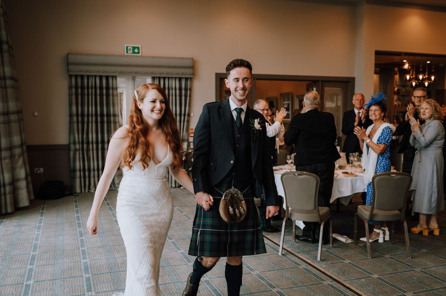 A couple making their entrance at a Scottish-themed wedding, with the groom wearing a traditional kilt.