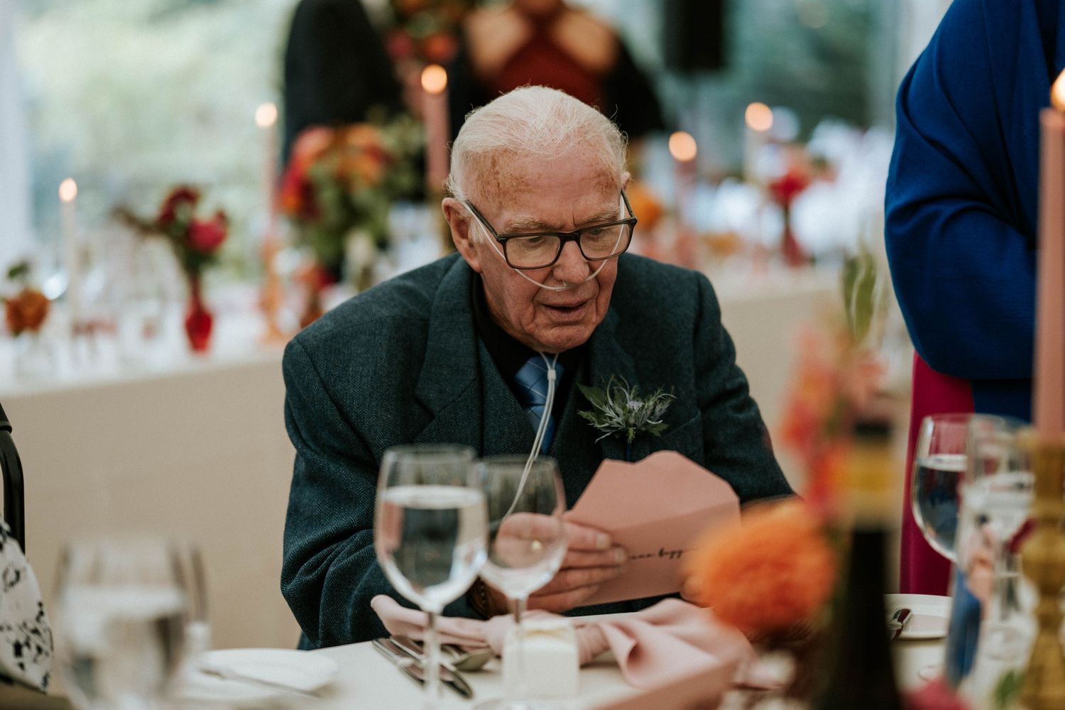 An elderly guest at a wedding reception reads something at the dining table.