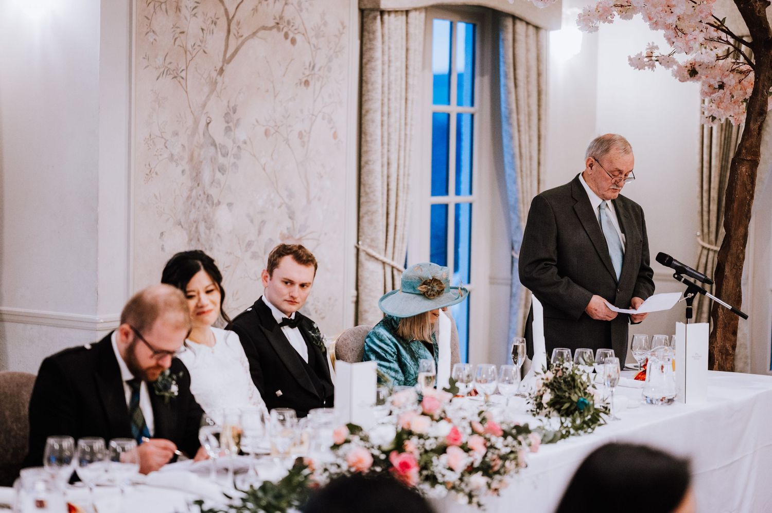 Formal dinner speech being given at elegant reception with floral centerpieces.