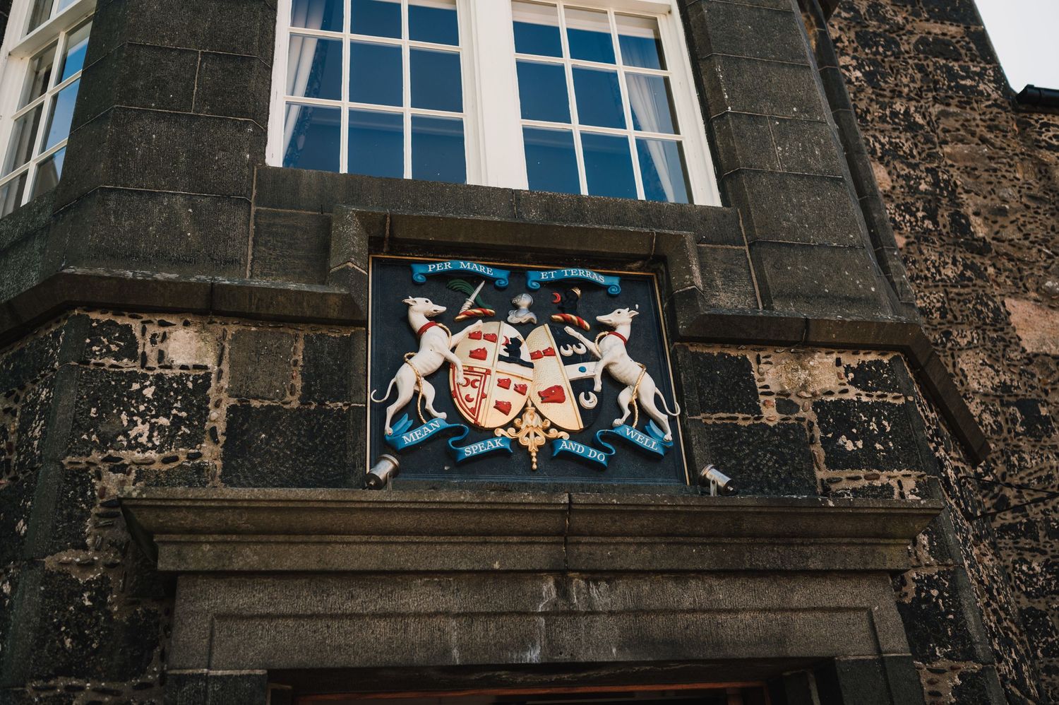 Ornate heraldic crest detail above a window on a stone building facade.