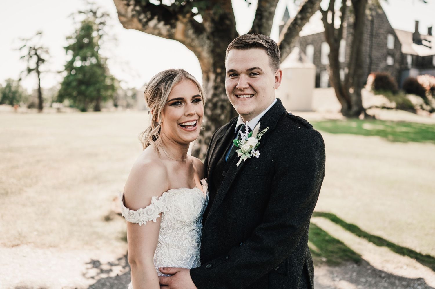 Joyful wedding portrait on sunny day with traditional Scottish attire.