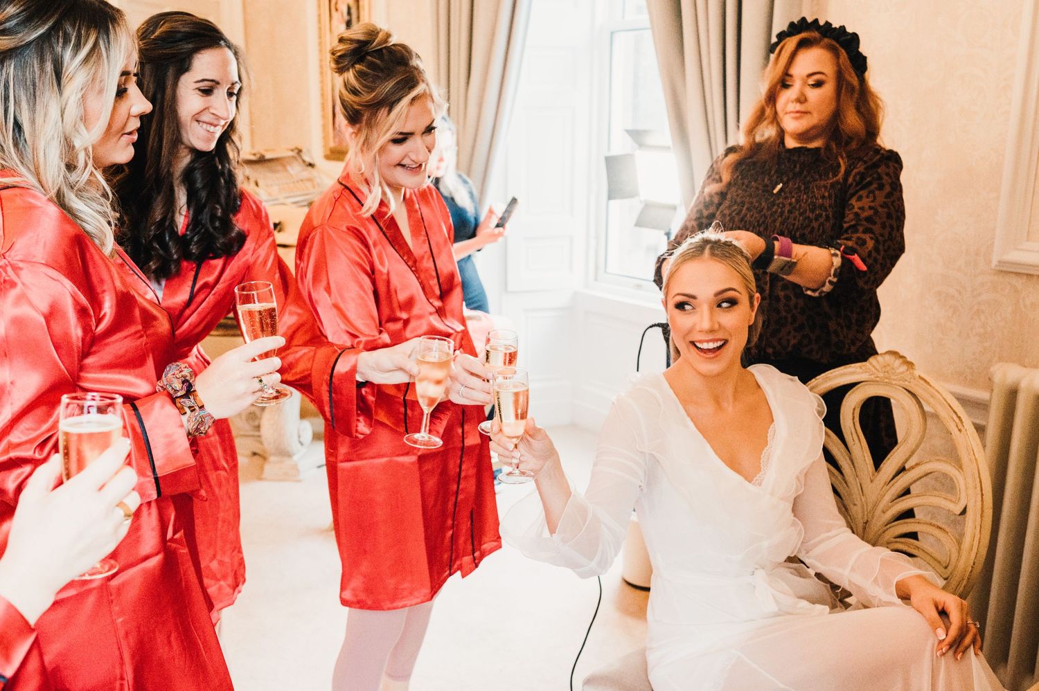 Bridal party in matching red silk robes during wedding morning preparations.