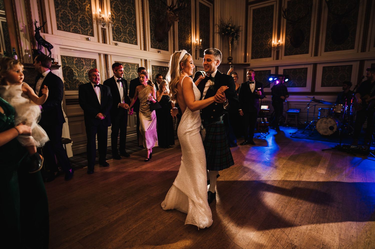 Wedding couple sharing their first dance on a hardwood floor surrounded by watching guests.