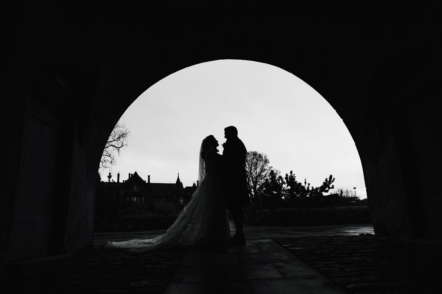 A silhouetted wedding couple standing in an archway creates a dramatic circular frame.