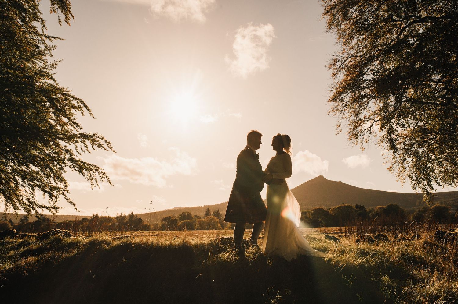 Sunset silhouette of wedding couple standing in mountain landscape.