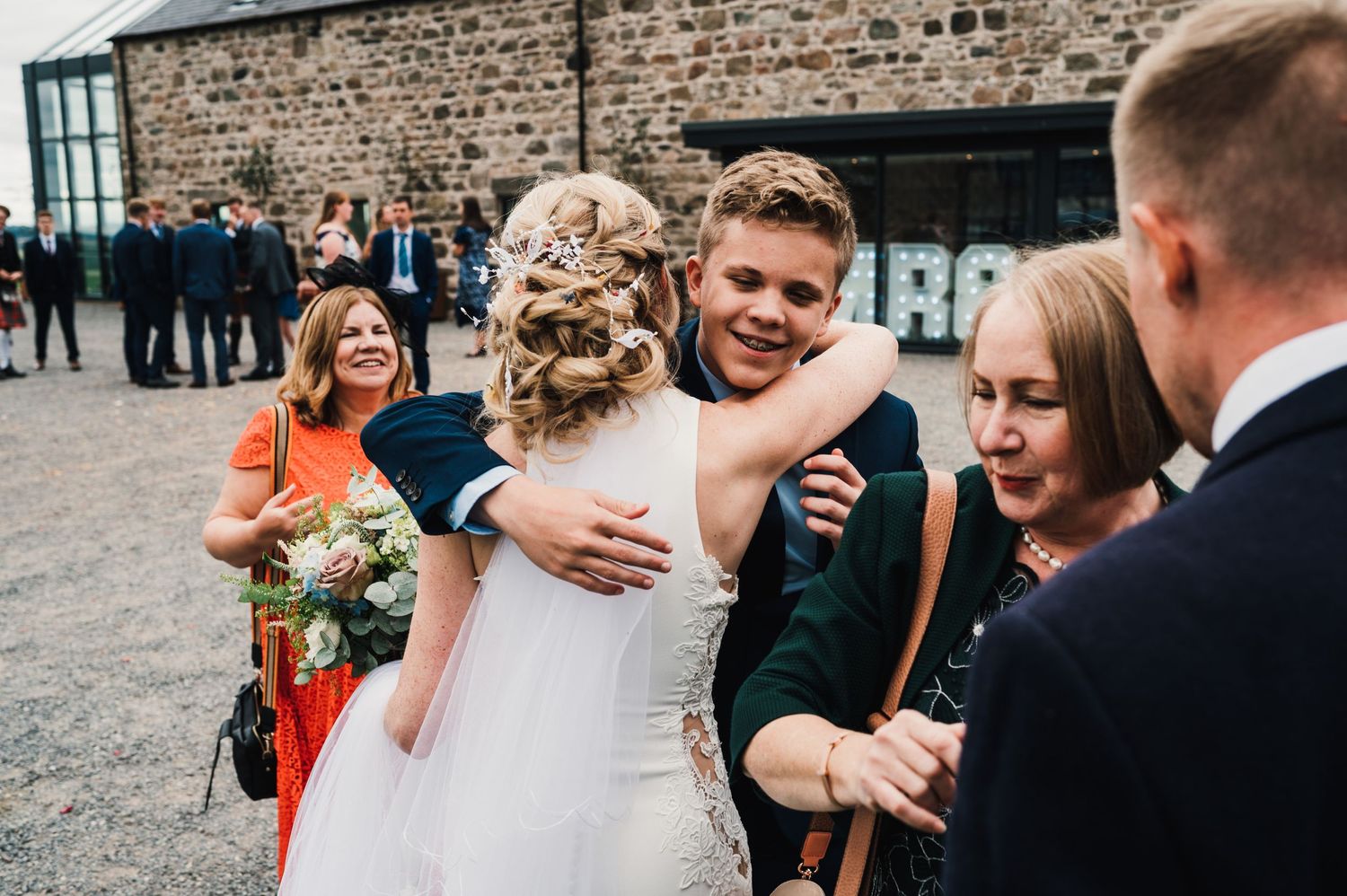 Joyful wedding celebration with guests sharing hugs outside rustic stone venue.