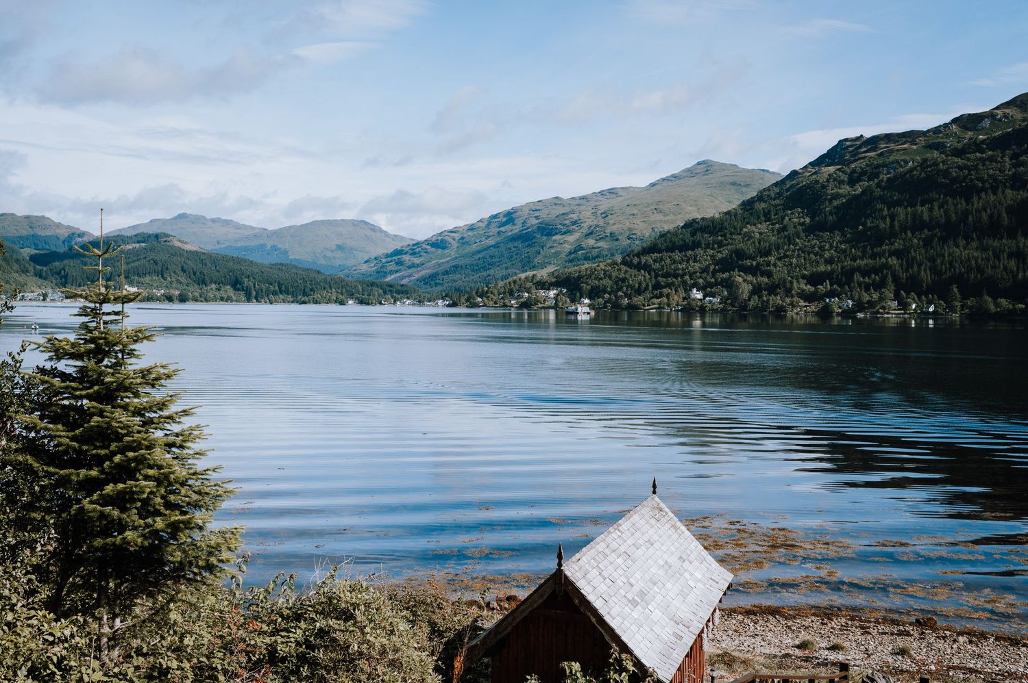 Peaceful mountain lake view with evergreen trees and distant peaks reflecting in calm waters.