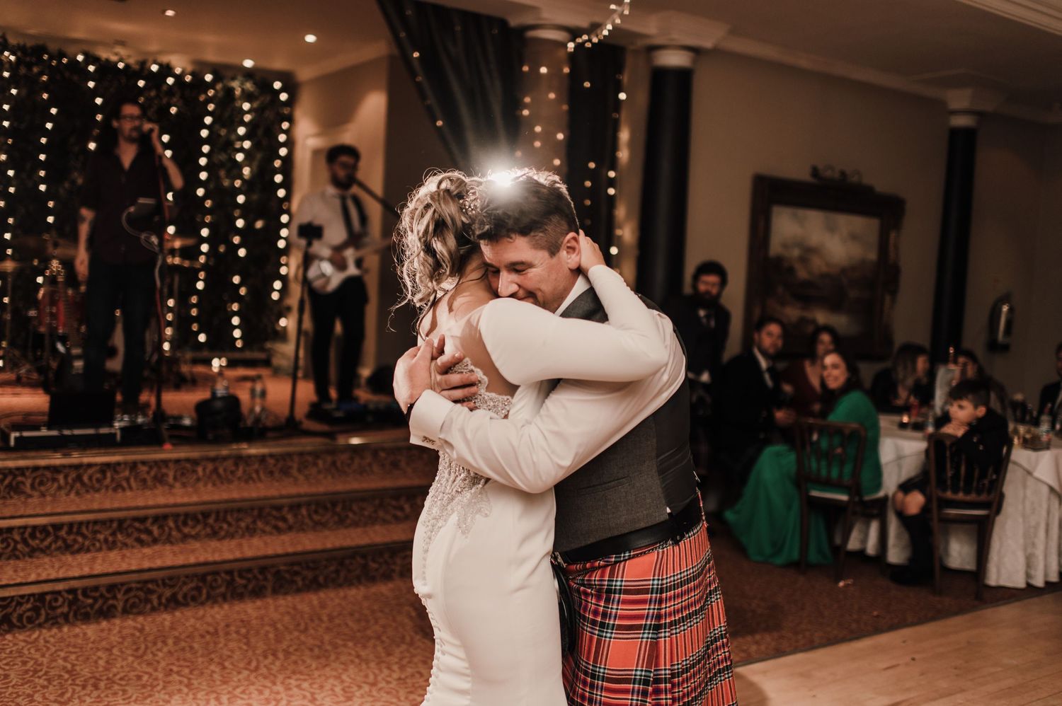 A tender embrace during a wedding dance with the groom in traditional Scottish kilt and bride in elegant white dress.
