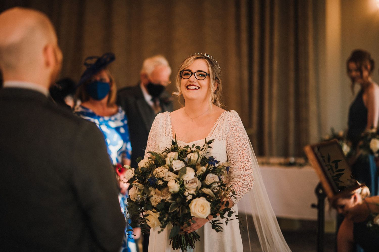 A joyful wedding scene showing a bouquet of white and green flowers during an indoor ceremony.