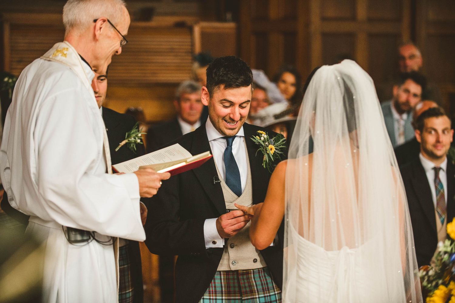 Clergy member reads from book during wedding ceremony while couple stands attentively.