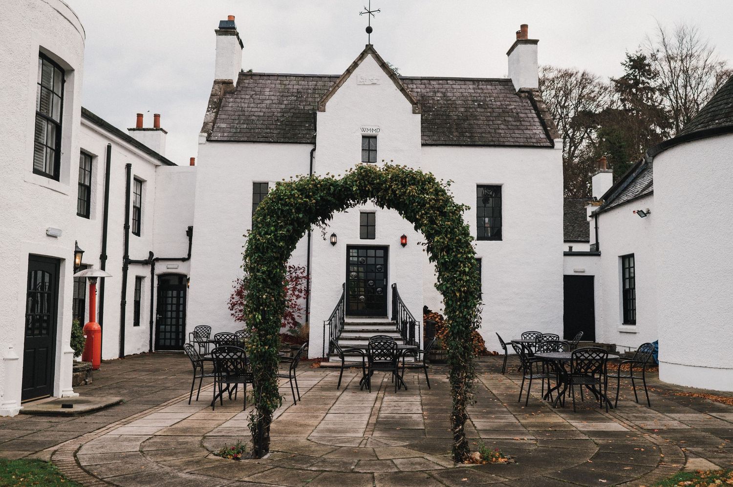 White stone building entrance with floral arch and outdoor seating area.