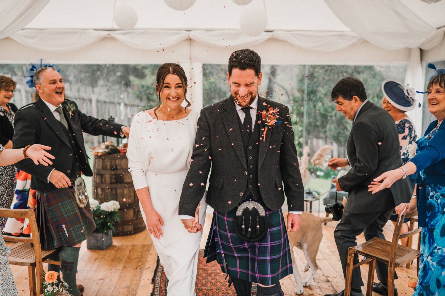 Wedding celebration in a tent with guests throwing confetti at the happy couple.