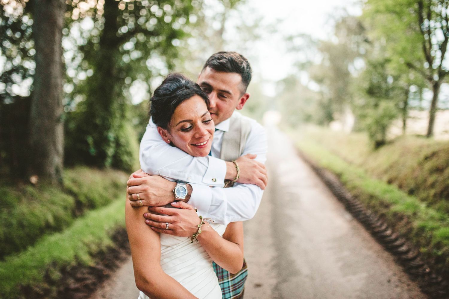 A couple embraces on a tree-lined country path during their wedding photoshoot.