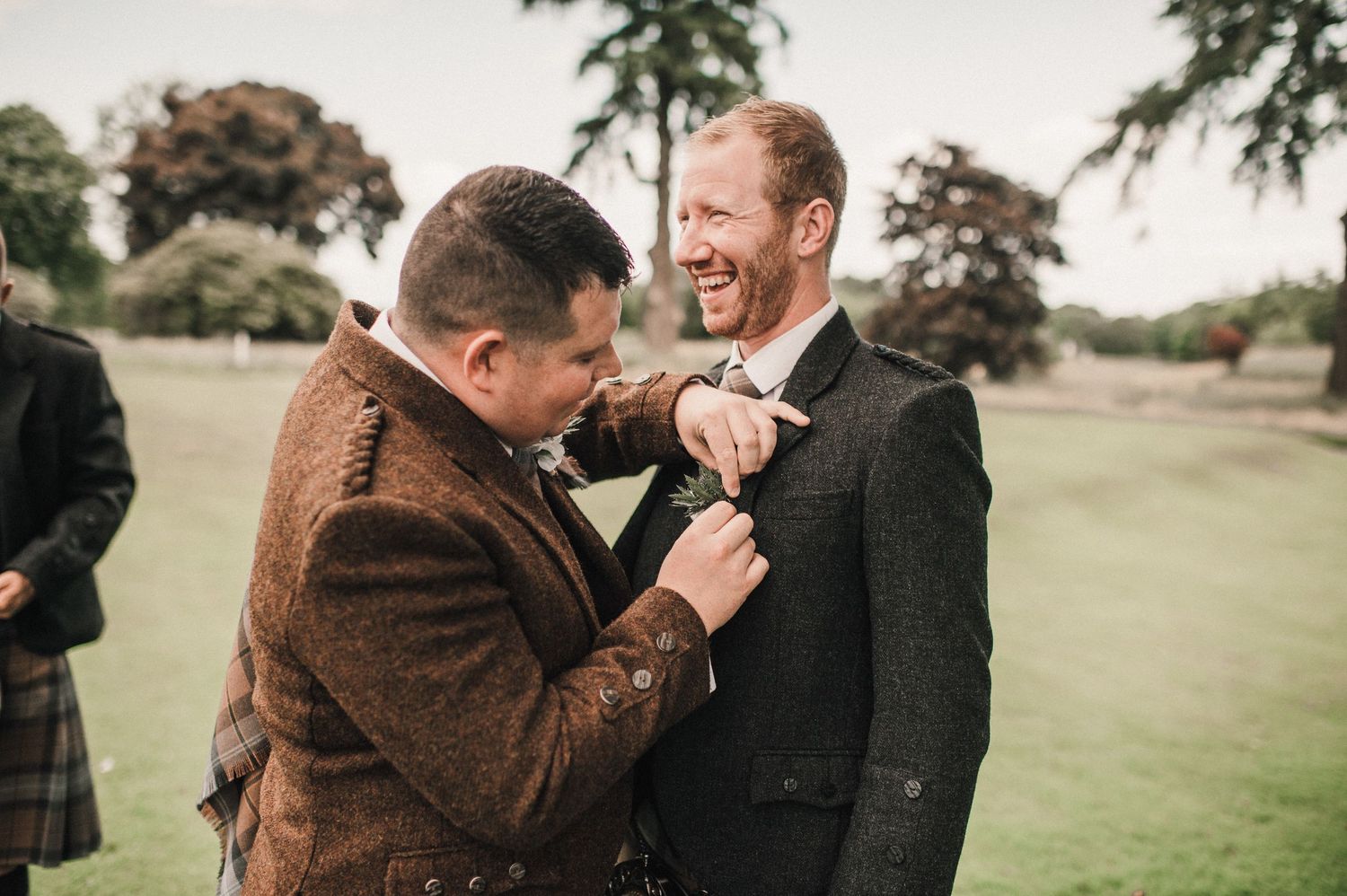 Two people laughing while adjusting their formal wear on a grassy lawn.
