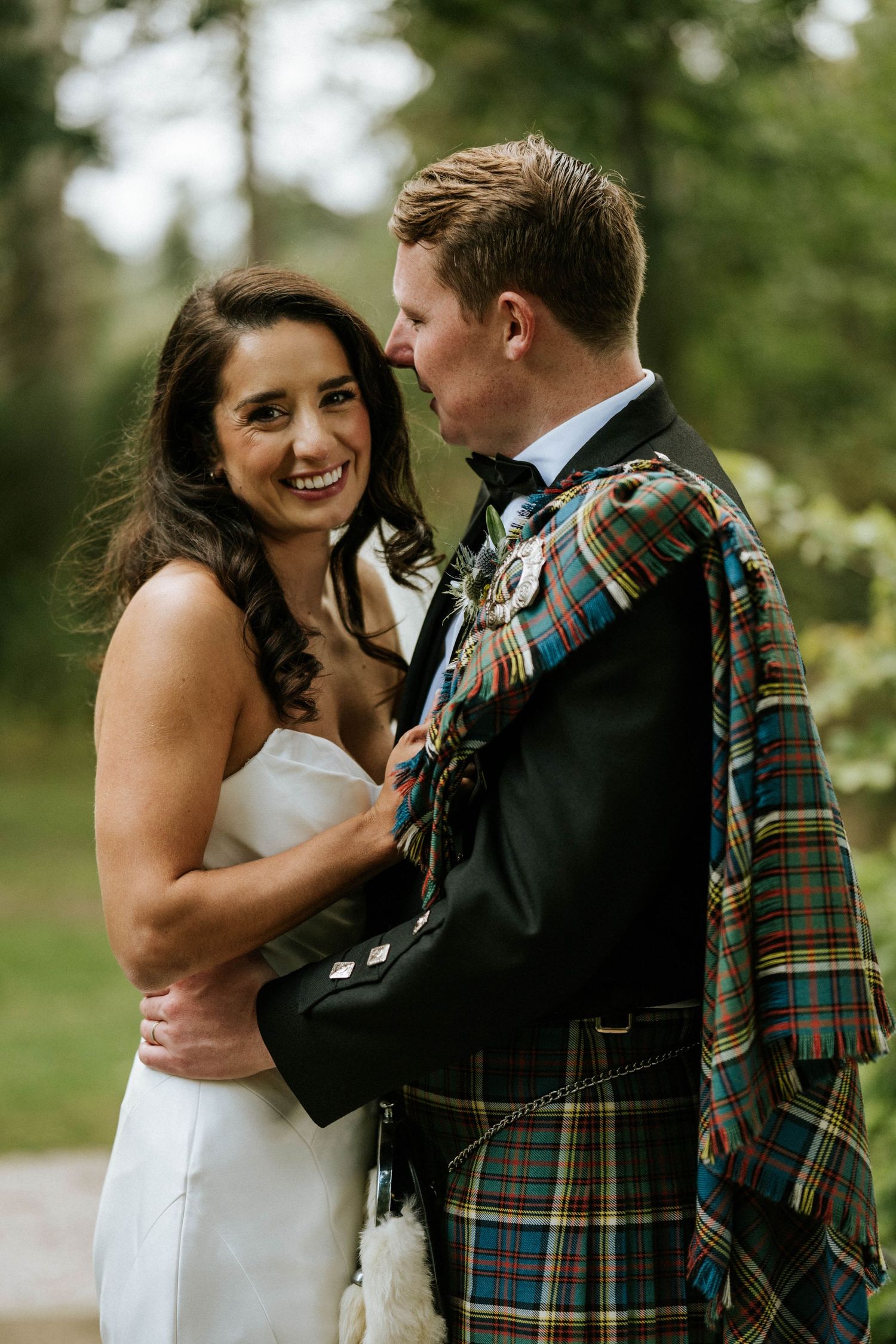 Wedding couple shares intimate moments while wearing traditional Scottish wedding attire in a garden setting.