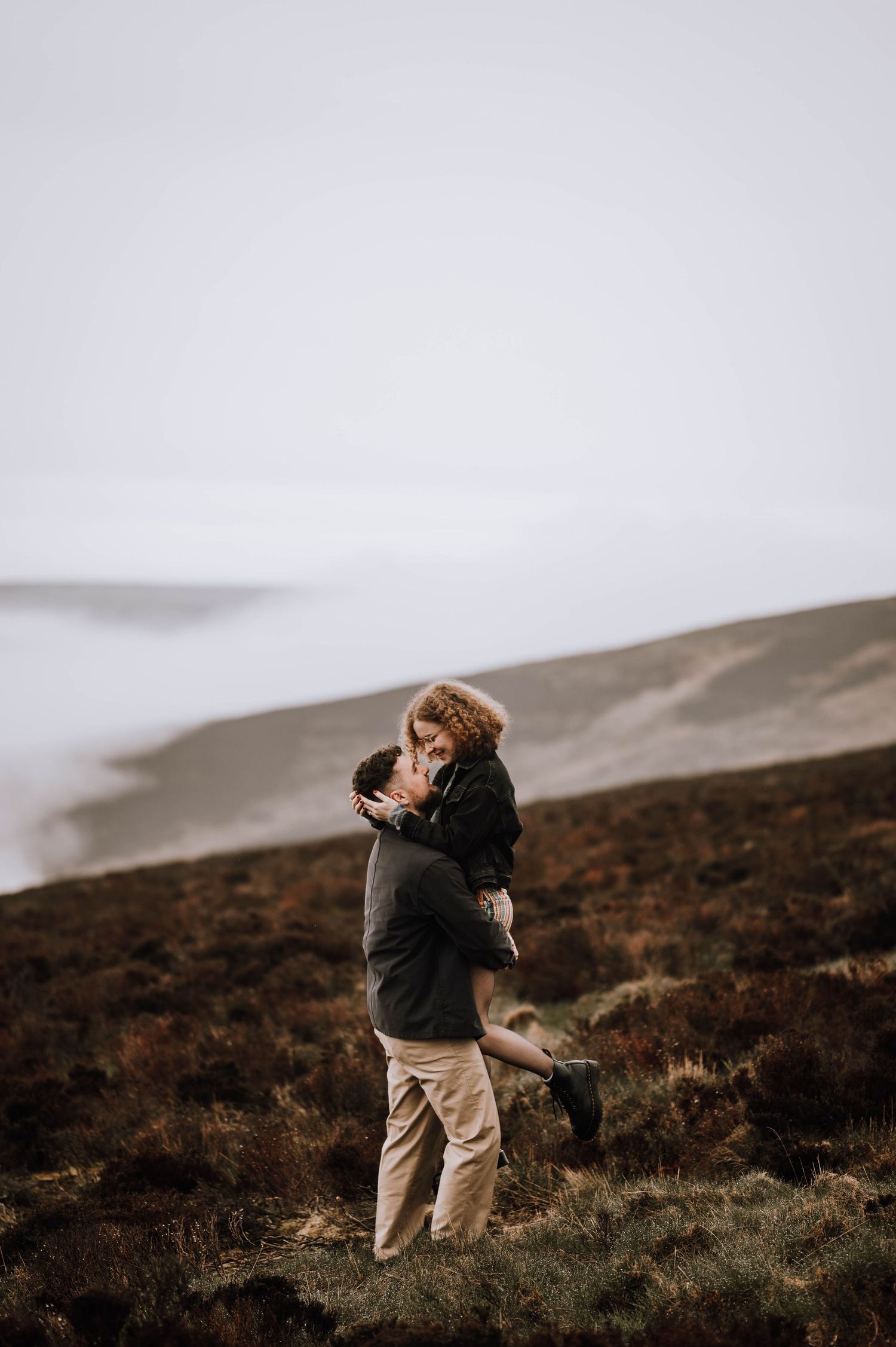 Engagement photography session Aberdeen. A couple embraces on a misty mountainside covered in heather and wild grass.