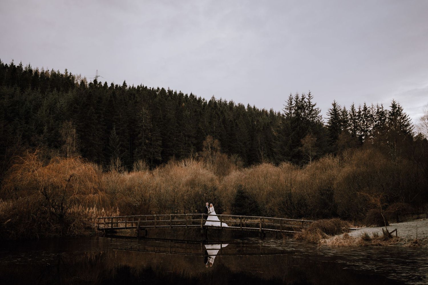 A white dress reflects on still water surrounded by dark woods and autumn foliage on a moody day.